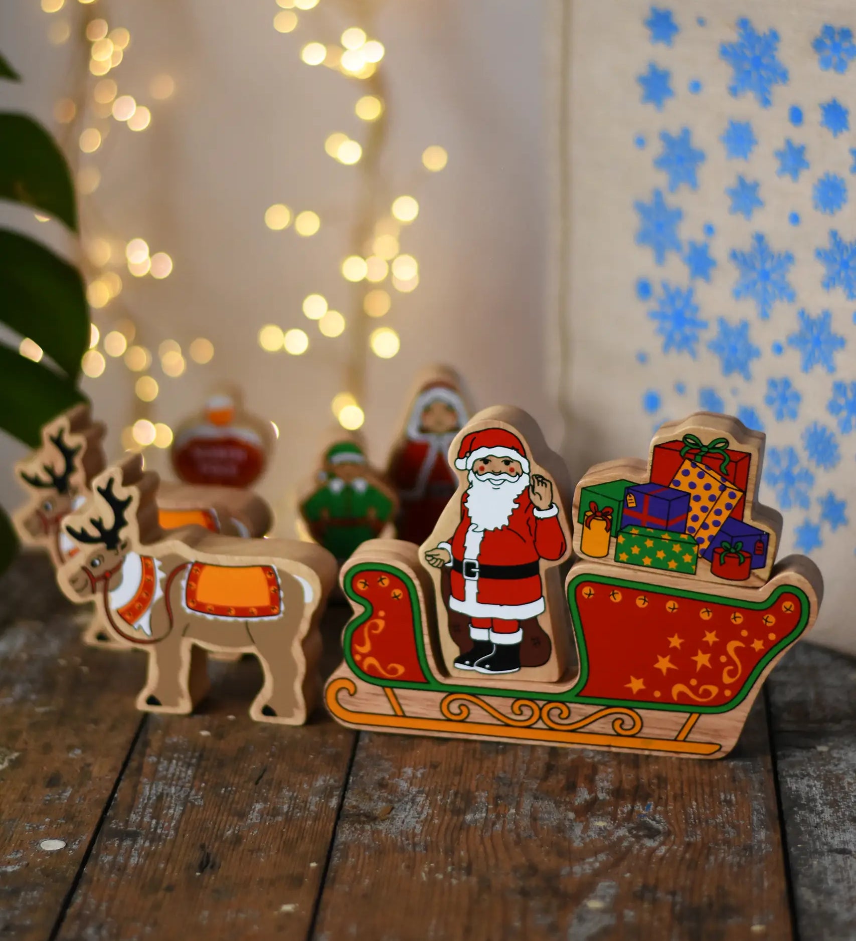 Lanka Kade wooden Christmas toy figures including Father Christmas,  red sleigh, Mrs Clause, North Pole Sign, Elf and 2 Reindeer placed on a wooden surface in the Babipur playroom.