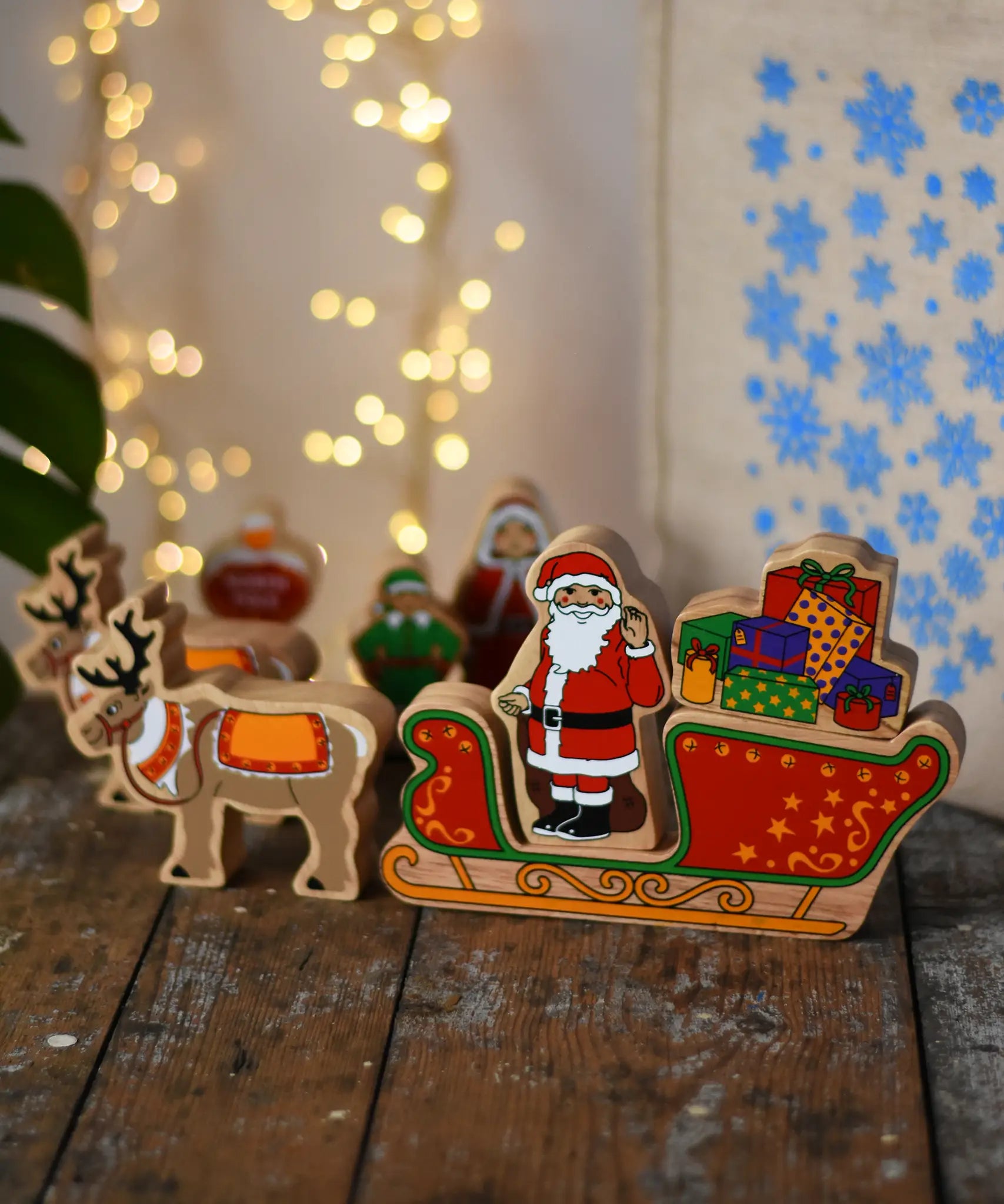 Lanka Kade wooden Christmas toy figures including Father Christmas,  red sleigh, Mrs Clause, North Pole Sign, Elf and 2 Reindeer placed on a wooden surface in the Babipur playroom.