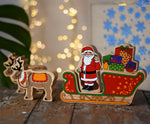 Lanka Kade wooden Christmas toy figures including Father Christmas, red sleigh, wrapped presents,and 2 Reindeer placed on a wooden surface in the Babipur playroom.