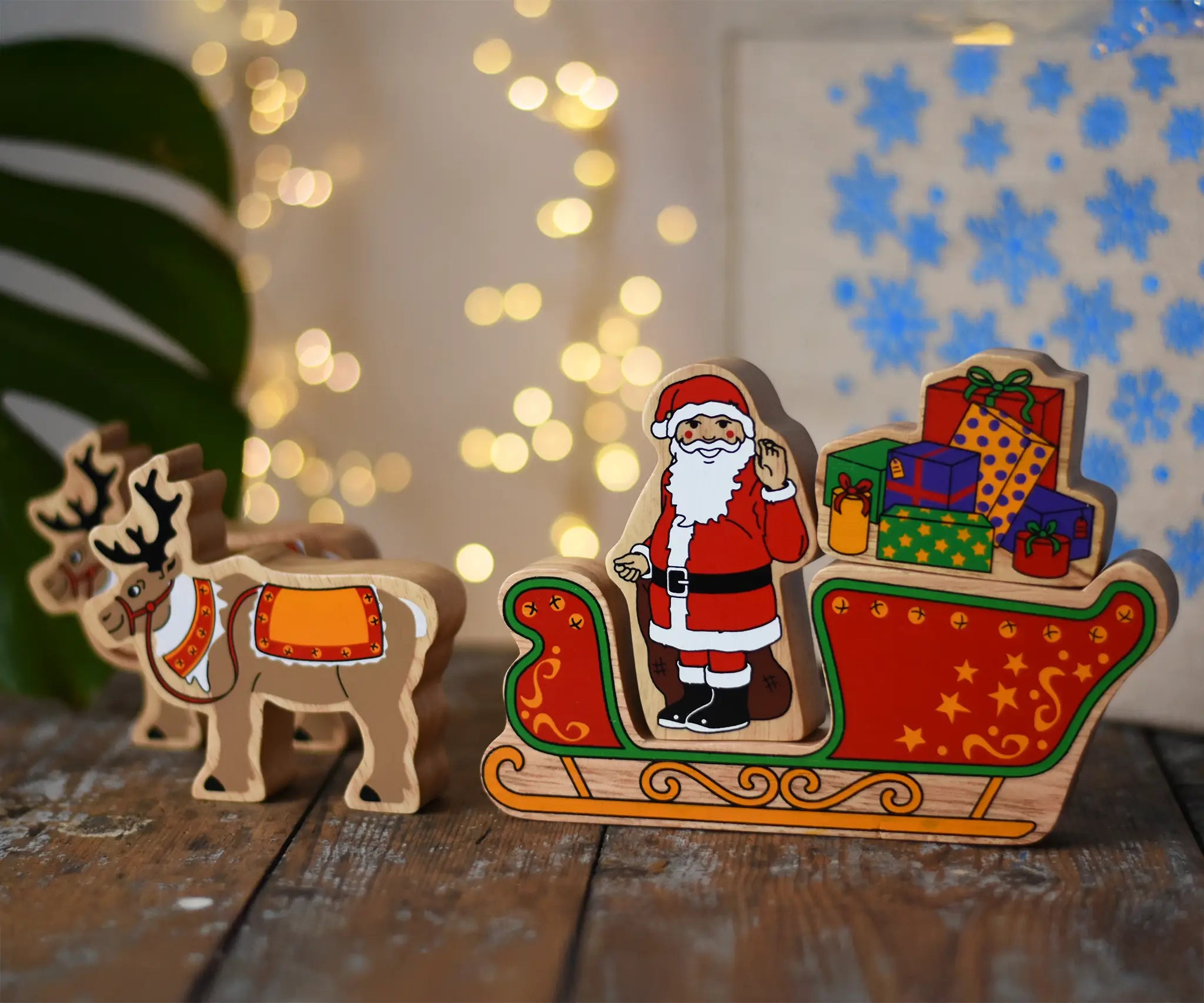 Lanka Kade wooden Christmas toy figures including Father Christmas, red sleigh, wrapped presents,and 2 Reindeer placed on a wooden surface in the Babipur playroom.