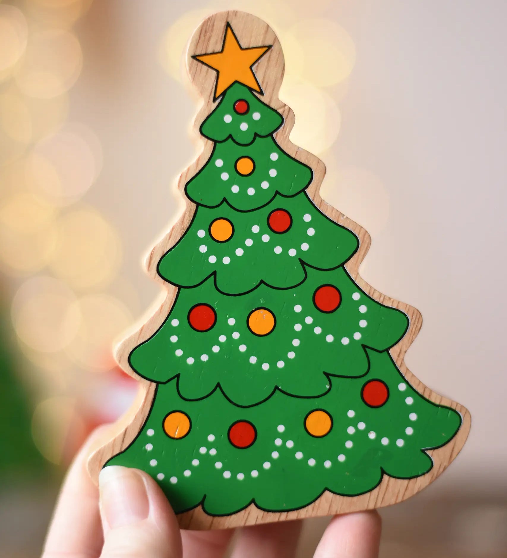 Lanka Kade Christmas tree wooden toy figure in an adult's hand. Green tree with red and yellow baubles and a yellow star on the top.