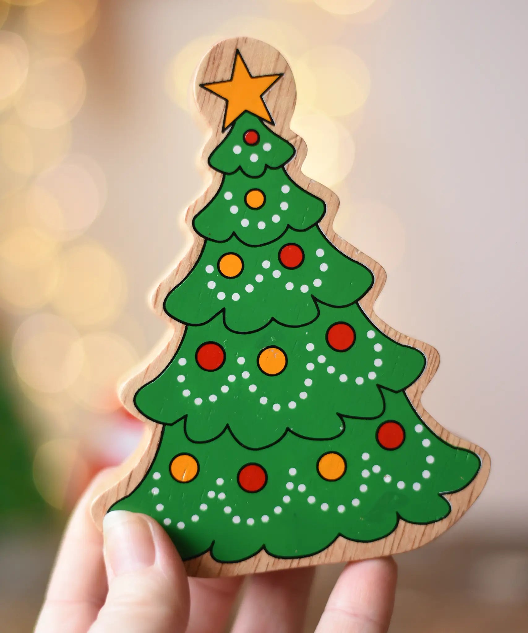 Lanka Kade Christmas tree wooden toy figure in an adult's hand. Green tree with red and yellow baubles and a yellow star on the top.