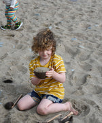 A child playing with Lanka Kade coconut bowls and utensils on the beach. 