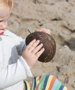 A young child pouring sand from a Lanka Kade coconut bowl on a beach. The Lanka Kade coconut collection is part of our wide range of outdoor toys here at Babipur. 