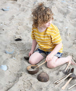 A child playing with Lanka Kade coconut bowls and utensils on the beach. 