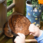 A close up of the Lanka Kade coconut shell colander bowl in a young child's hand. The bowl appears shiny as it's just been taken out of water and is wet.