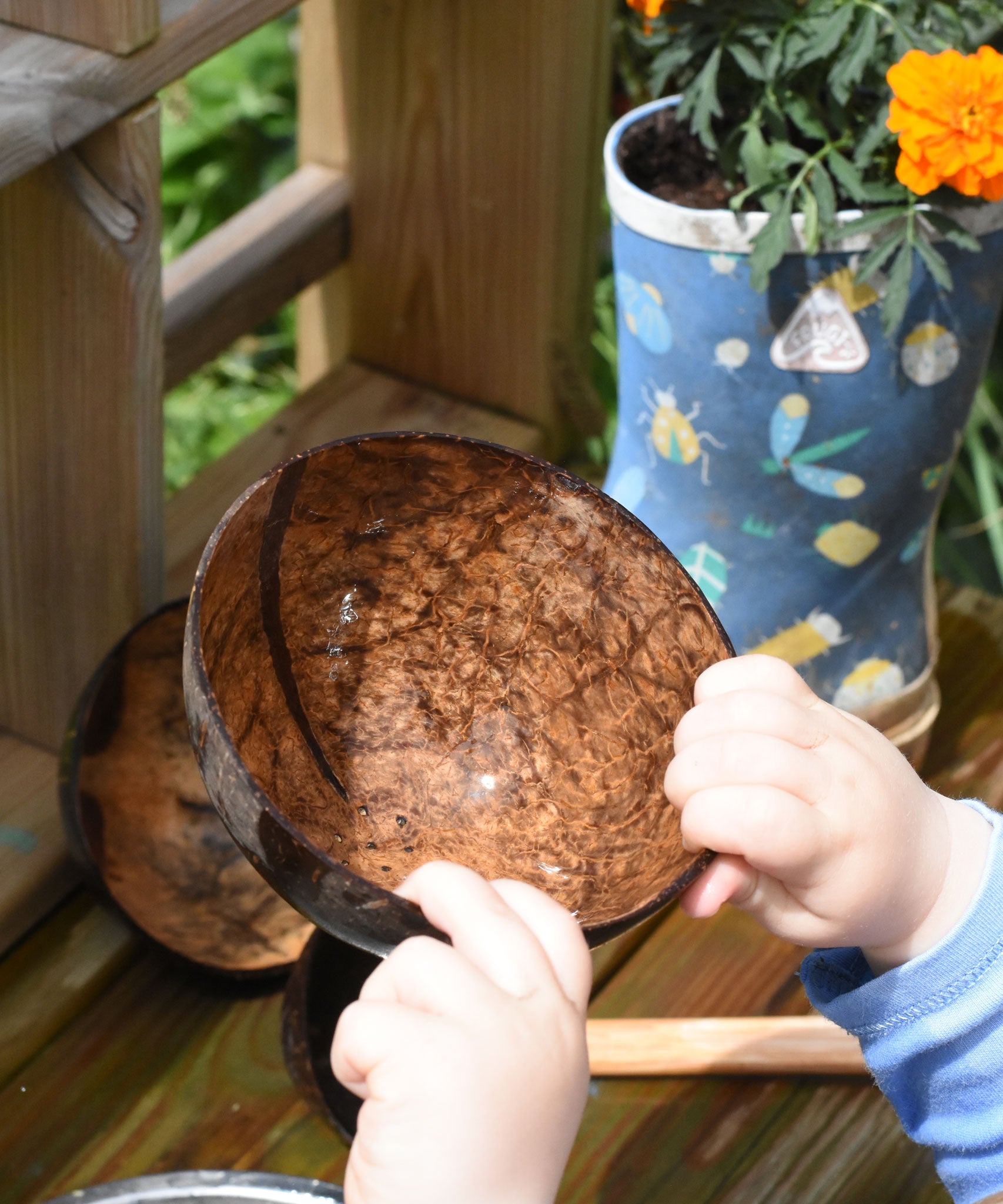 A close up of the Lanka Kade coconut shell colander bowl in a young child's hand. The bowl appears shiny as it's just been taken out of water and is wet.