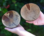 Two coconut shell bowls in a child's hand. One bowl has holes in it to allow for water or sand to flow through. 