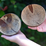Two coconut shell bowls in a child's hand. One bowl has holes in it to allow for water or sand to flow through. 