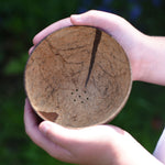 A close up of a Lanka Kade coconut shell colander bowl in a child's hands. 