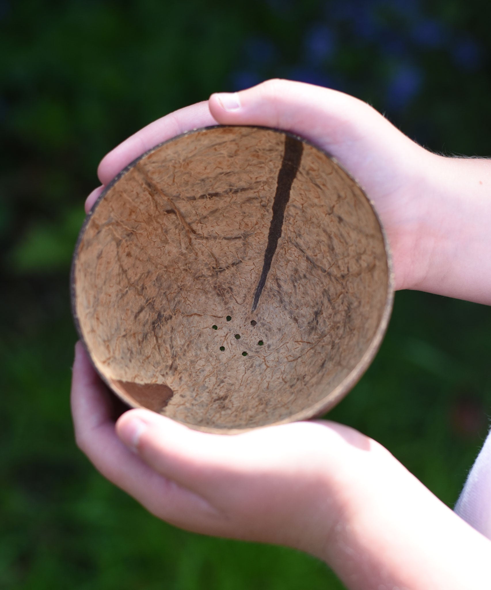 A close up of a Lanka Kade coconut shell colander bowl in a child's hands. 