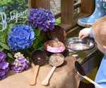 A child playing with the Lanka Kade coconut shell utensils set in an outdoor mud kitchen.