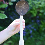 A close up of a Lanka Kade coconut shell slotted spoon in a child's hand..