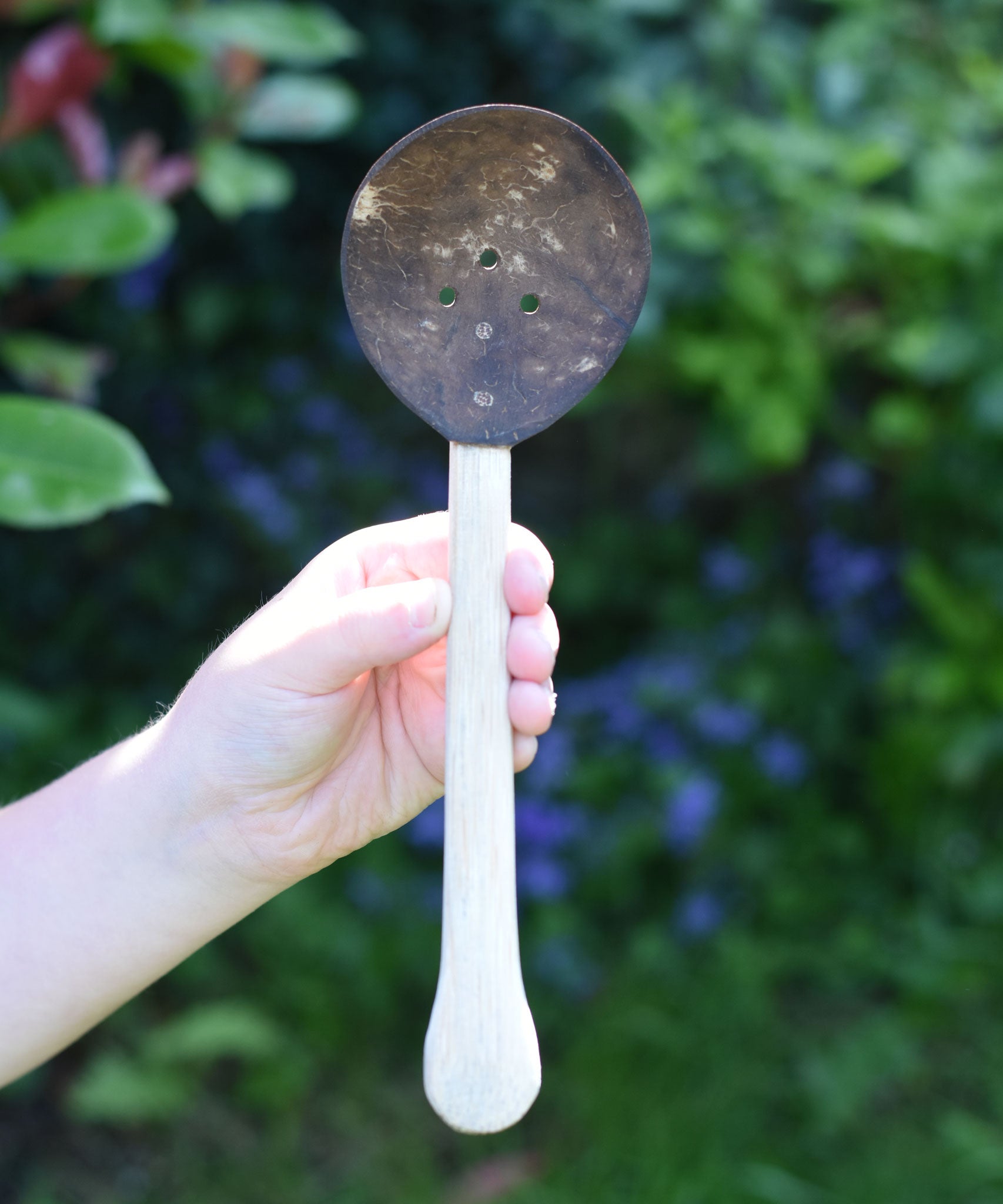 A close up of a Lanka Kade coconut shell slotted spoon in a child's hand..