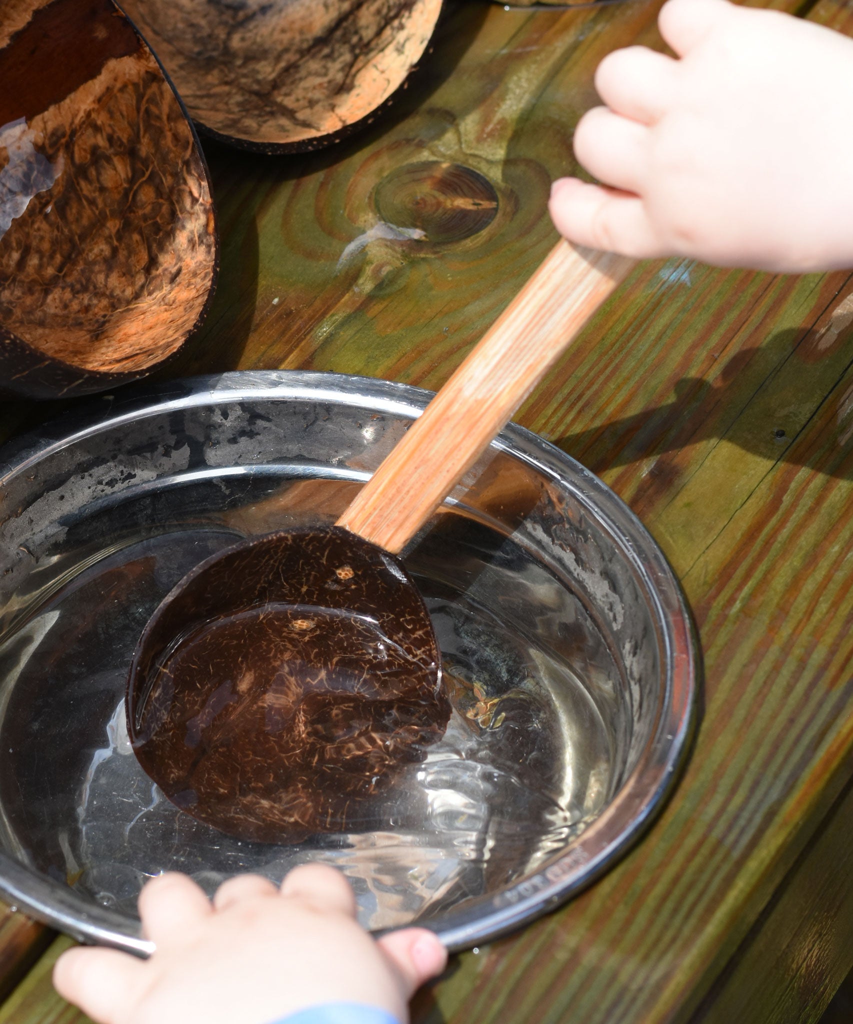 A close up of a child using the Lanka Kade coconut shell spoon utensil. The child is scooping water out of a small water bowl.