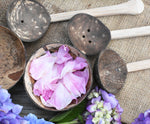 A top down view of the coconut shell bowl filled with pink peony petals. The other bowl and the coconut shell utensils from the Lanka Kade water play set can be seen around it.