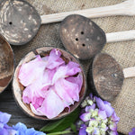 A top down view of the coconut shell bowl filled with pink peony petals. The other bowl and the coconut shell utensils from the Lanka Kade water play set can be seen around it.
