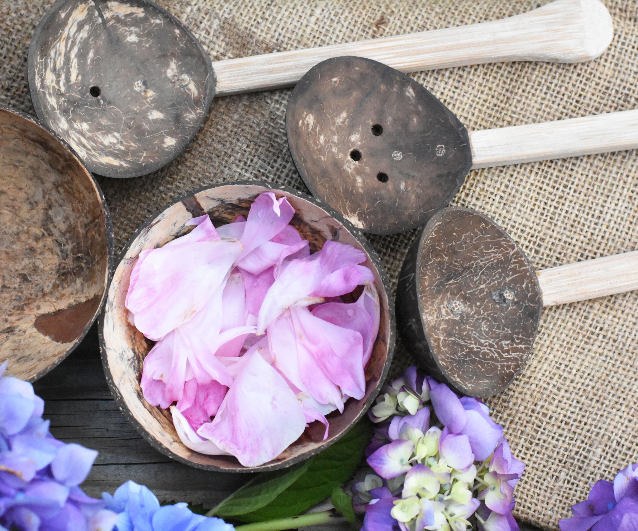 A top down view of the coconut shell bowl filled with pink peony petals. The other bowl and the coconut shell utensils from the Lanka Kade water play set can be seen around it.