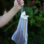 The Lanka Kade Coconut Shell Water Playset held up in a child's hand. The utensils and bowls have all been placed in a white mesh storage bag that come with the set.  