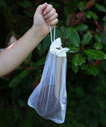 The Lanka Kade Coconut Shell Water Playset held up in a child's hand. The utensils and bowls have all been placed in a white mesh storage bag that come with the set.  