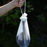 The Lanka Kade Coconut Shell Water Playset held up in a child's hand. The utensils and bowls have all been placed in a white mesh storage bag that come with the set.  