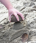 An upturned Lanka Kade coconut bowl being emptied of sand. A dome of sand has been created.