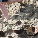 Lanka Kade coconut bowls and utensils placed on sand on a beach. A child can be seen running past in the background with bits of sand in the air as he goes past.