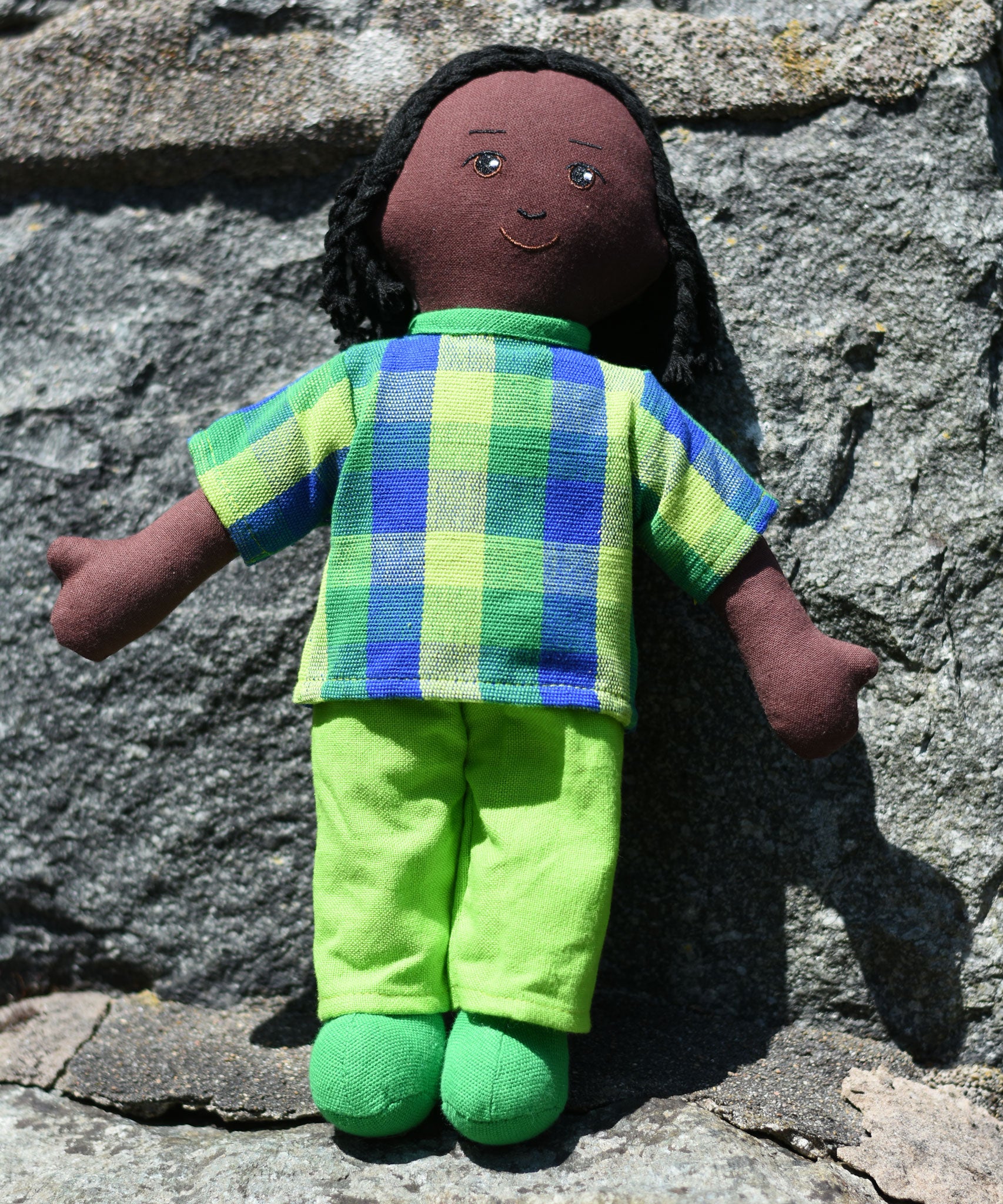 A Lanka Kade Rag Doll Dad - Black Skin, Black Hair placed on a stone wall outdoors. 