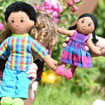 A close up of a child holding up a Lanka Kade dad doll with brown skin and black hair next to an adult holding up a girl doll with brown skin and black hair. 