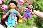 A close up of a child holding up a Lanka Kade dad doll with brown skin and black hair next to an adult holding up a girl doll with brown skin and black hair. 