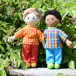 Two Lanka Kade Fair Traded dad dolls placed on a slate surface outdoors. One has white skin and blonde hair the other has brown skin and black hair.
