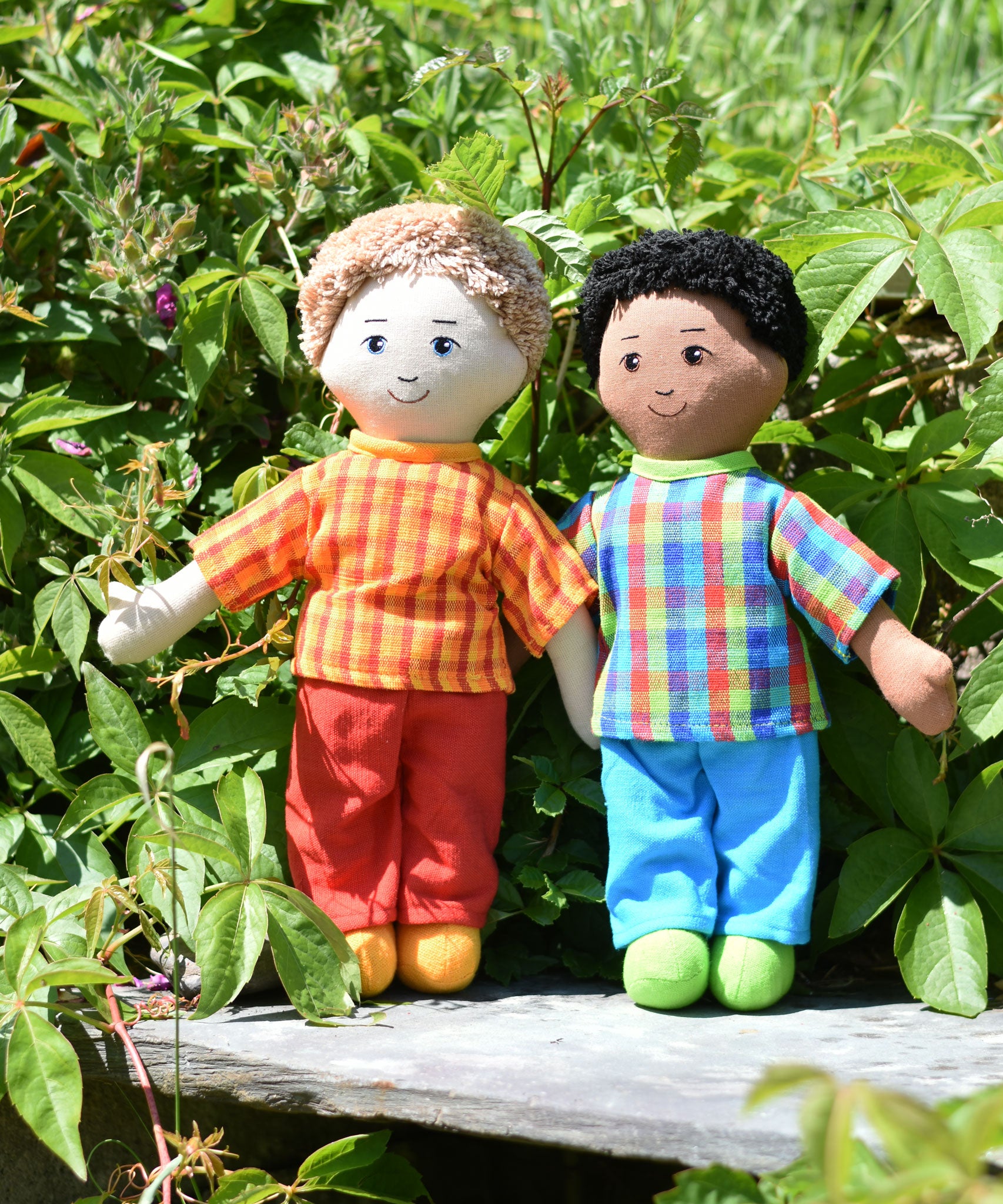 Two Lanka Kade Fair Traded dad dolls placed on a slate surface outdoors. One has white skin and blonde hair the other has brown skin and black hair.