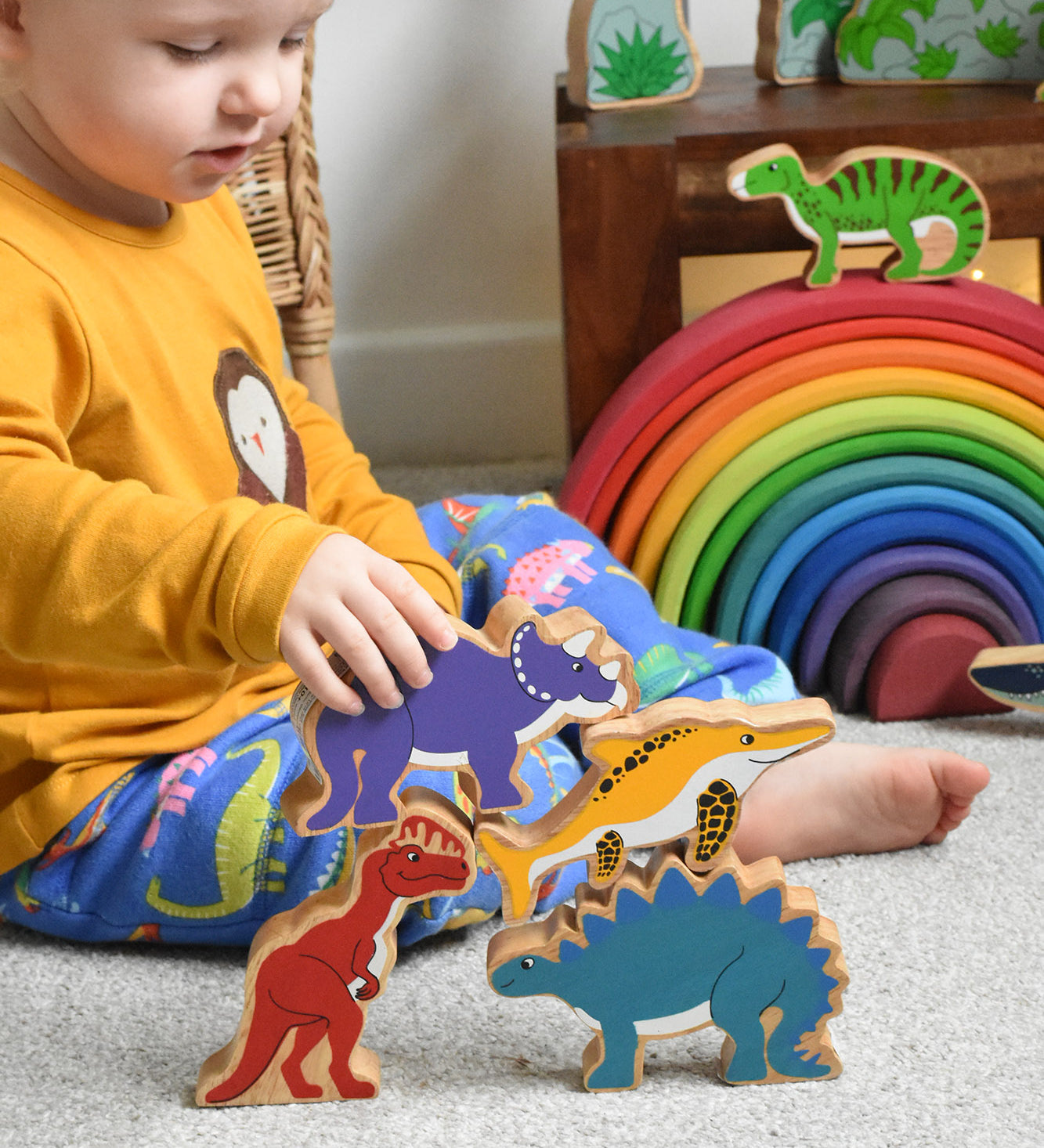A child playing with Lanka Kade wooden toy animal figures. The child has his hand on a purple dinosaur figure. These wooden toy figures are part of a huge range of Lanka Kade fair trade, wooden toys available here at Babipur.