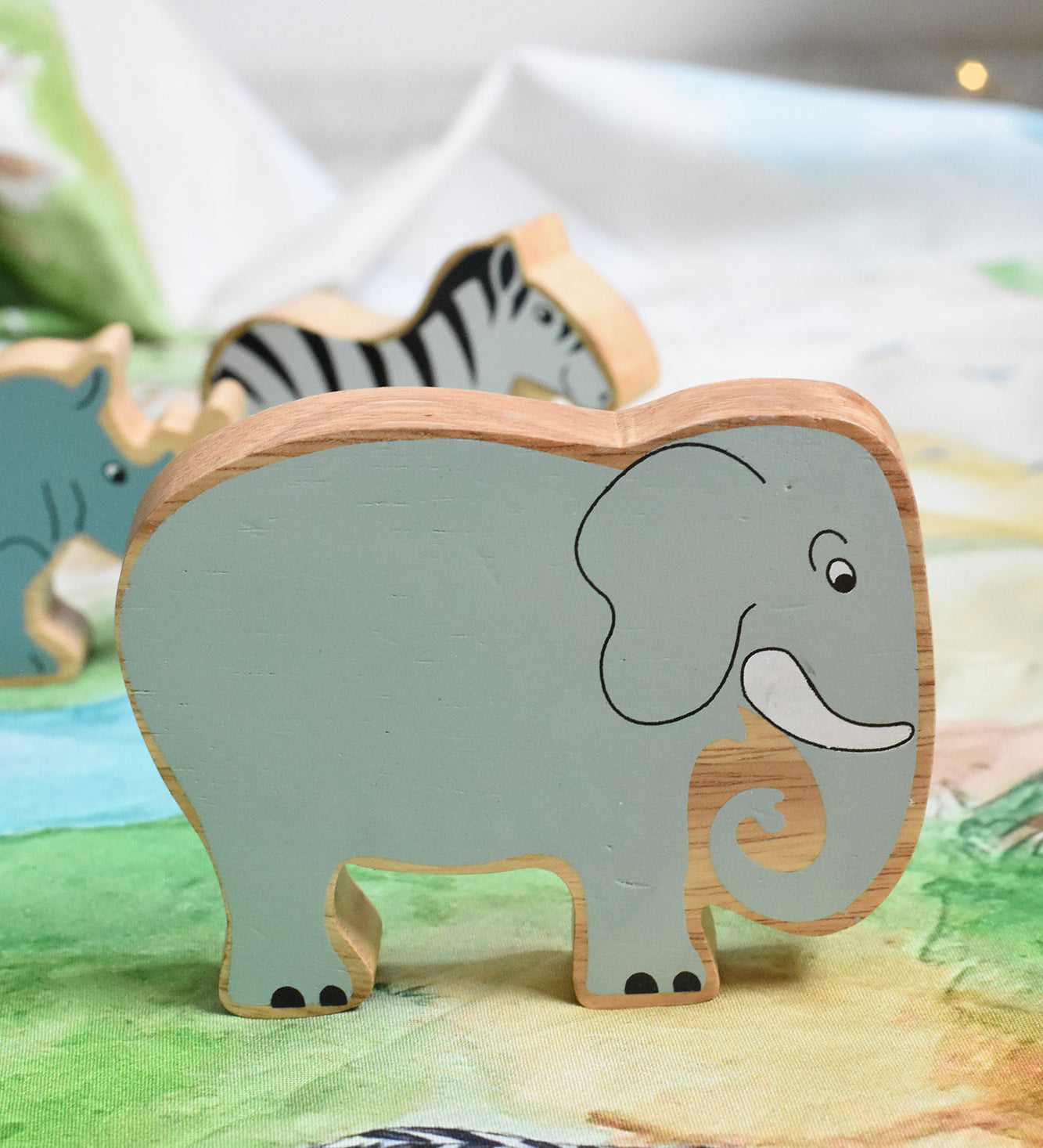 A Lanka Kade grey elephant wooden toy figure placed on a Wonderie plains of Africa play cloth. These wooden toy figures are part of a huge range of Lanka Kade fair trade, wooden toys available here at Babipur.