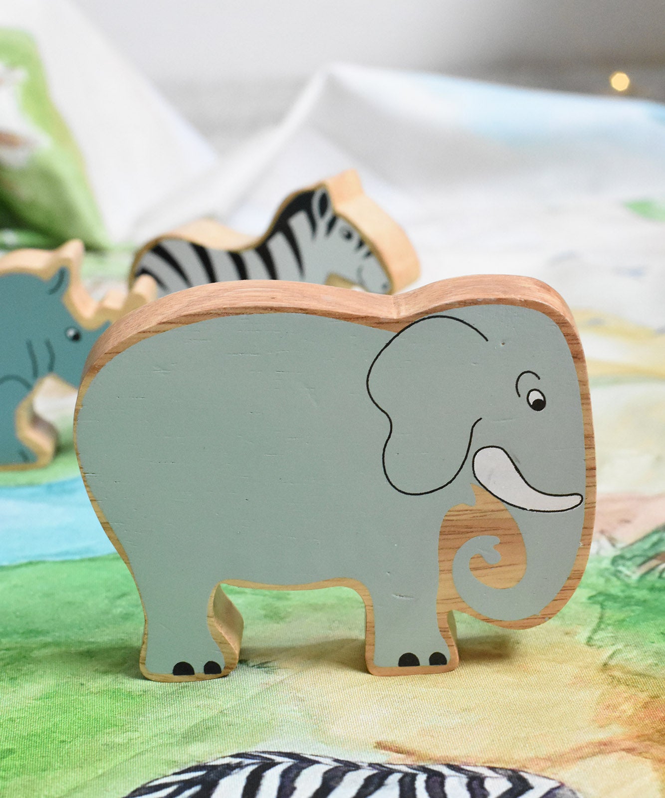 A Lanka Kade grey elephant wooden toy figure placed on a Wonderie plains of Africa play cloth. These wooden toy figures are part of a huge range of Lanka Kade fair trade, wooden toys available here at Babipur.