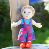A Lanka Kade Boy Doll with White Skin and Blonde Hair leaning against a wooden fence post.