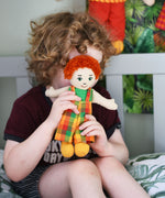 A child holding a Lanka Kade Boy Doll with White Skin and Red Hair.