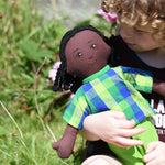 A close up of a Lanka Kade Rag Doll Dad - Black Skin, Black Hair in a child's arms.