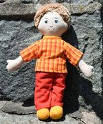 A Fair Trade Lanka Kade Dad doll on a stone wall. The doll has white skin and blonde hair and is wearing a t-shirt and trousers made from sari material offcuts. 