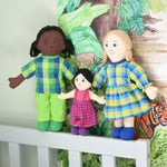 A family of Lanka Kade dolls leaning on a grey coloured headboard of a bed. There is a dad with black skin and balck hair, a girl with white skin and black hair and a mum doll with white skin and blonde hair. 