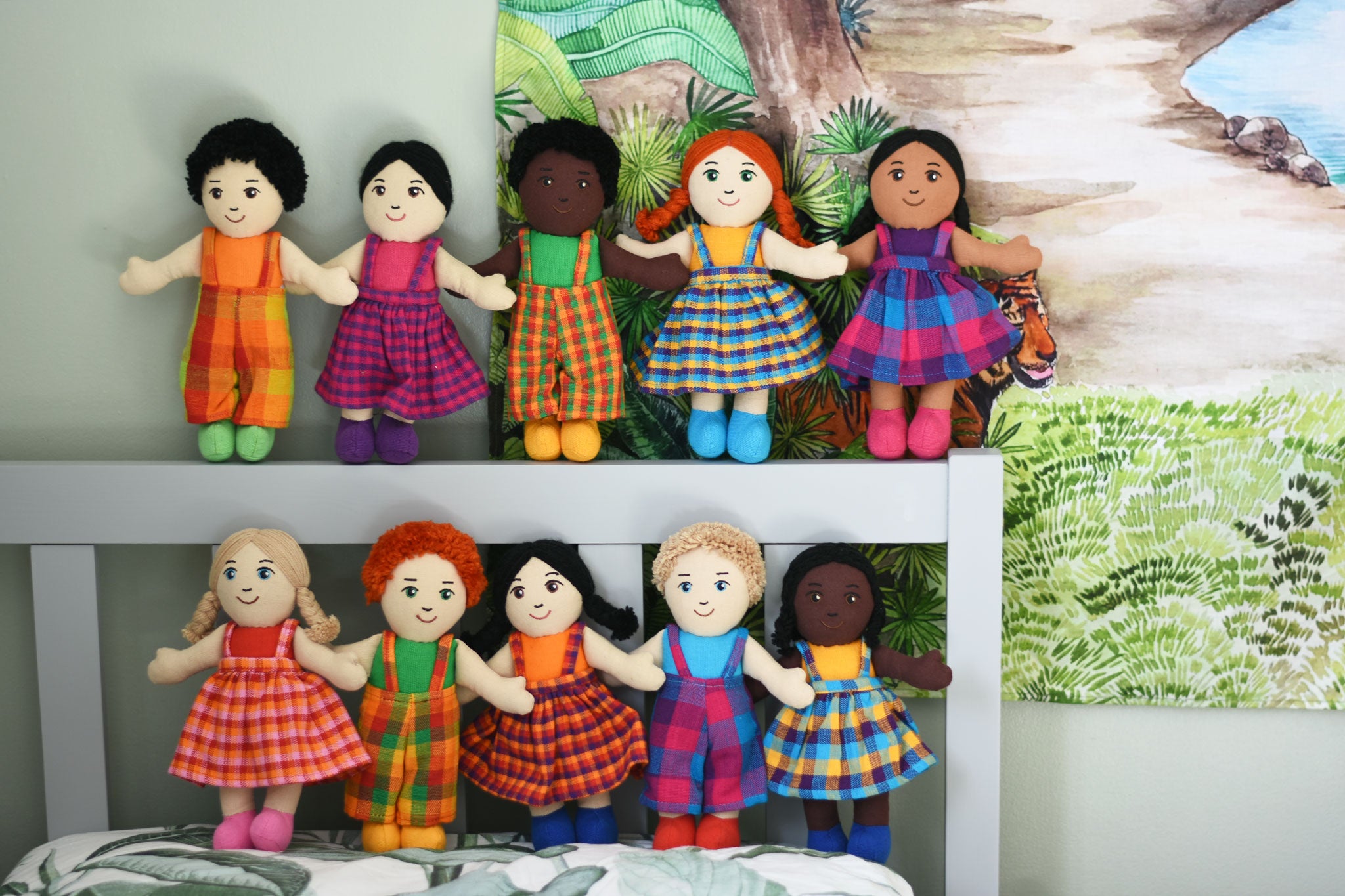A line up of 10 Lanka Kade Fair Trade boy and girl rag dolls. they have been paced on the pillow and headboard of a bed.