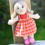 A Lanka Kade Girl Doll with White Skin and Blonde Hair leaning against a wooden post outdoors.