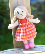 A Lanka Kade Girl Doll with White Skin and Blonde Hair leaning against a wooden post outdoors.