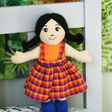 A Lanka Kade Girl Doll with White Skin and Black Hair placed on a pillow, leaning against a headboard..