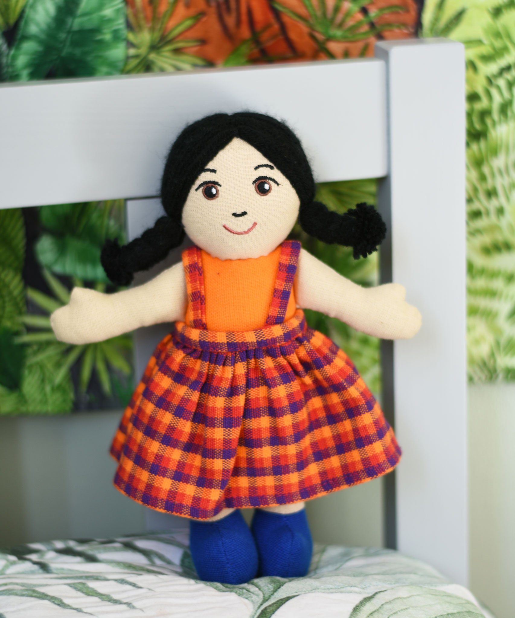 A Lanka Kade Girl Doll with White Skin and Black Hair placed on a pillow, leaning against a headboard..
