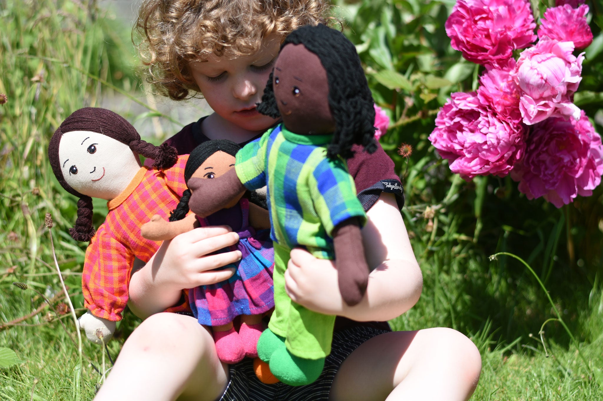 A child holding three Lanka Kade Rag Dolls in their arms a Mum with White Skin and Black Hair, a dad with black hair and skin and a child with brown skin and black hair.