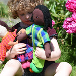 A child holding three Lanka Kade Rag Dolls in their arms a Mum with White Skin and Black Hair, a dad with black hair and skin and a child with brown skin and black hair.