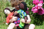 A child holding three Lanka Kade Rag Dolls in their arms a Mum with White Skin and Black Hair, a dad with black hair and skin and a child with brown skin and black hair.
