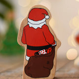 Back of the Lanka Kade Father Christmas wooden wooden toy figure placed on a wooden surface in the Babipur playroom. Santa is holding a brown sack filled with wrapped gifts.