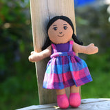 A Lanka Kade Girl Doll with Brown Skin and Black Hair leaning against a wooden post outdoors.